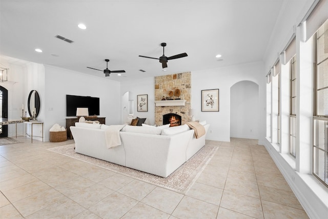 tiled living room featuring a stone fireplace, ceiling fan, and ornamental molding