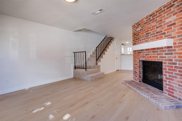 unfurnished living room featuring light wood-type flooring and a brick fireplace