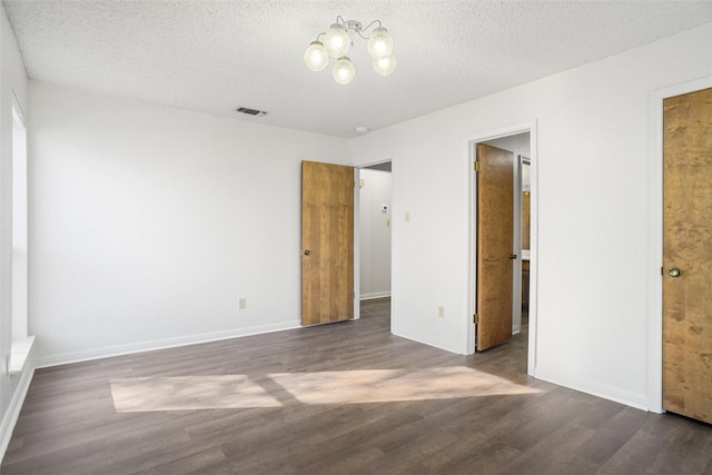 unfurnished bedroom featuring a notable chandelier, dark hardwood / wood-style floors, and a textured ceiling