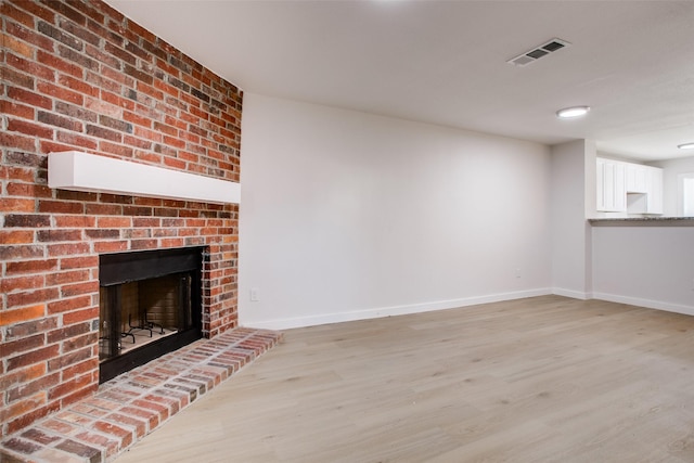 unfurnished living room featuring light hardwood / wood-style flooring and a brick fireplace