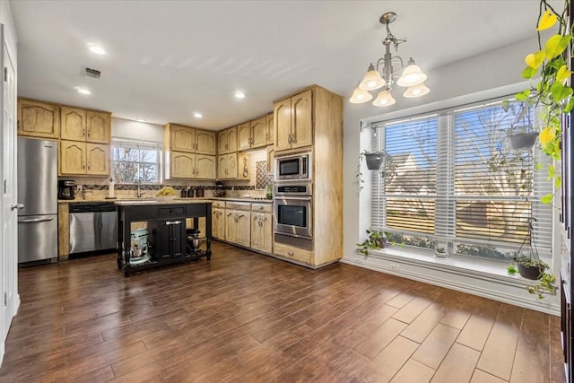 kitchen featuring appliances with stainless steel finishes, light brown cabinets, an inviting chandelier, backsplash, and hanging light fixtures