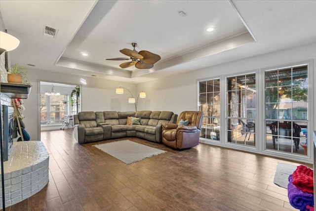 living room with dark wood-type flooring, ceiling fan with notable chandelier, and a tray ceiling