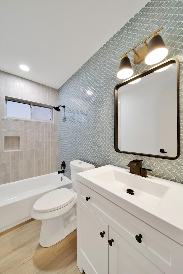 full bathroom featuring vanity, tiled shower / bath, hardwood / wood-style flooring, toilet, and tile walls