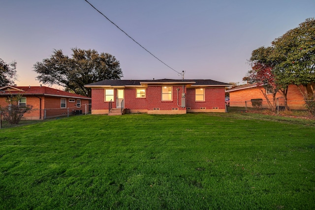 back house at dusk featuring a lawn