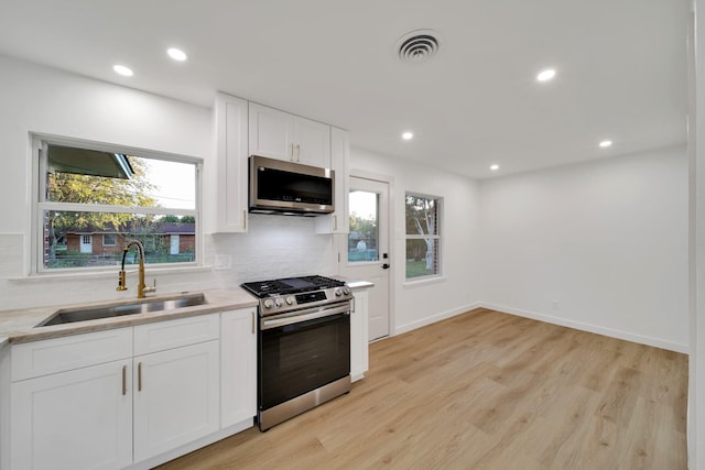 kitchen with a healthy amount of sunlight, white cabinets, sink, appliances with stainless steel finishes, and light hardwood / wood-style floors