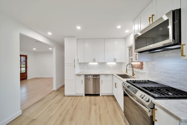 kitchen featuring sink, light hardwood / wood-style floors, decorative backsplash, white cabinets, and appliances with stainless steel finishes