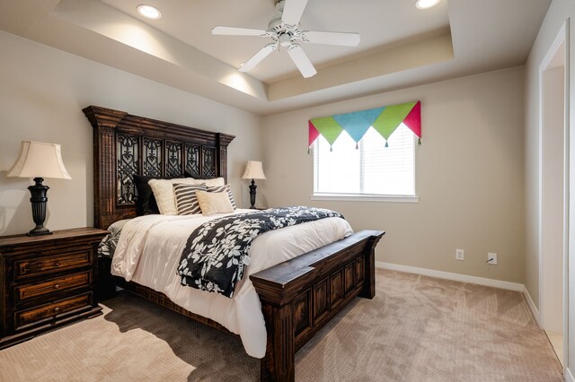 bedroom with light colored carpet, ceiling fan, and a tray ceiling