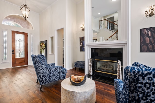 interior space featuring dark hardwood / wood-style floors, a towering ceiling, a tiled fireplace, ornamental molding, and an inviting chandelier