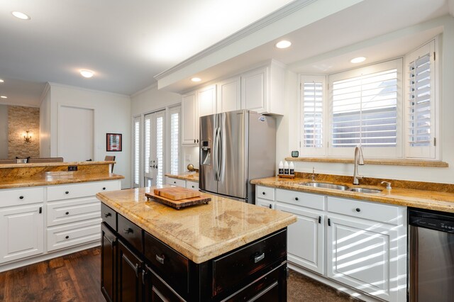 kitchen with appliances with stainless steel finishes, sink, white cabinets, ornamental molding, and a healthy amount of sunlight