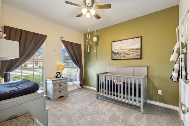 carpeted bedroom with a crib and ceiling fan