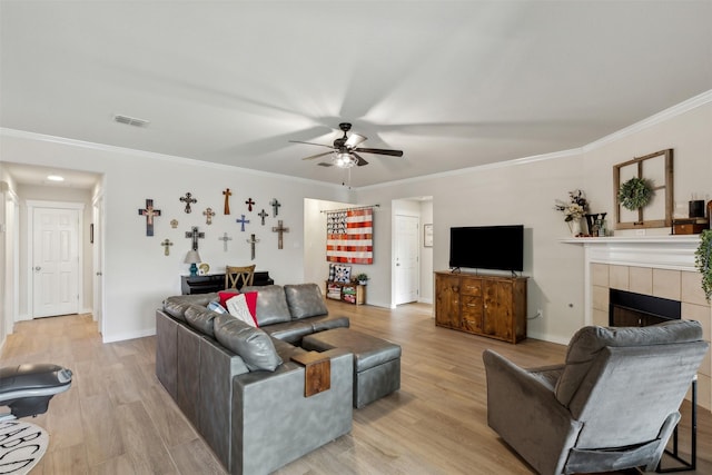 living room featuring crown molding, a tiled fireplace, light hardwood / wood-style flooring, and ceiling fan