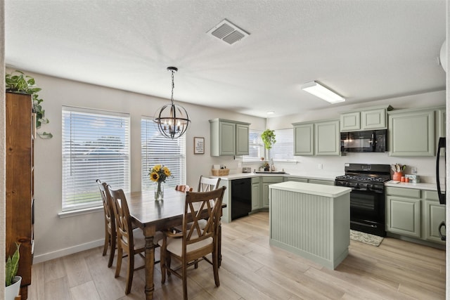 kitchen with black appliances, a chandelier, a kitchen island, light hardwood / wood-style flooring, and pendant lighting