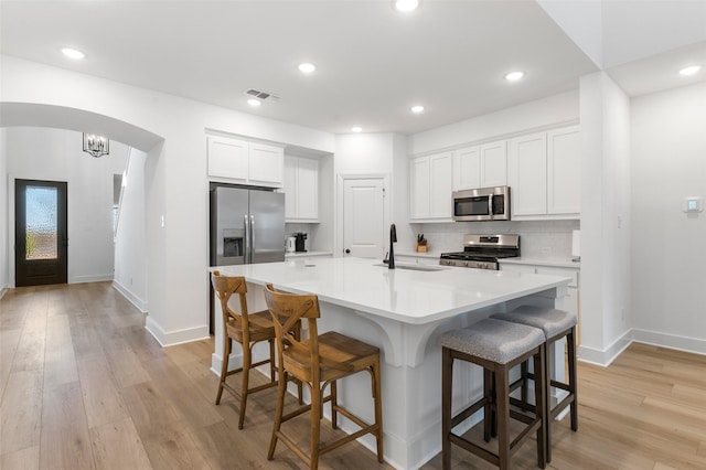 kitchen featuring a kitchen bar, white cabinetry, a center island with sink, and stainless steel appliances