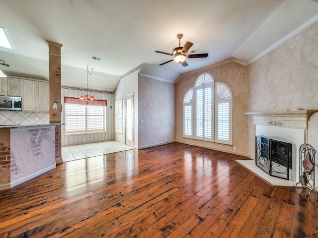 unfurnished living room featuring ceiling fan with notable chandelier, a fireplace, lofted ceiling, ornamental molding, and light hardwood / wood-style floors