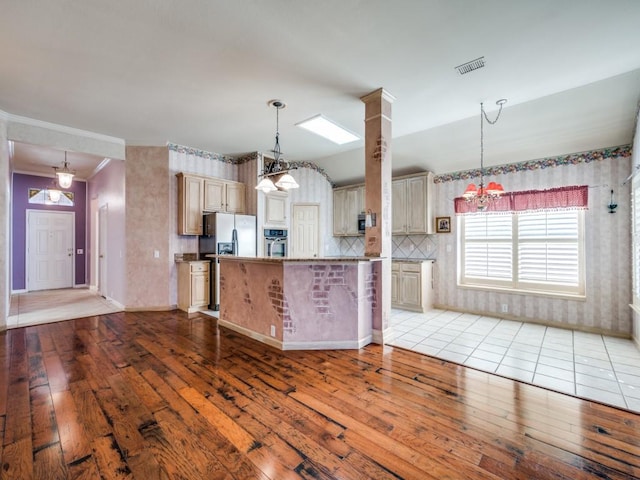 kitchen with appliances with stainless steel finishes, hanging light fixtures, light hardwood / wood-style floors, and decorative backsplash