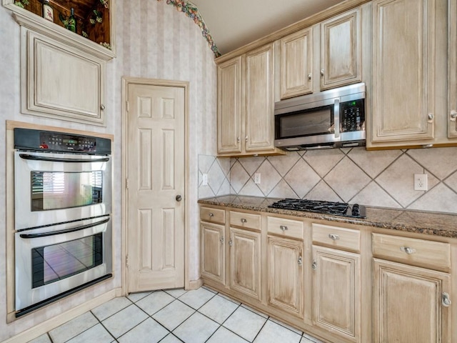 kitchen with stone countertops, light brown cabinets, light tile patterned floors, stainless steel appliances, and backsplash