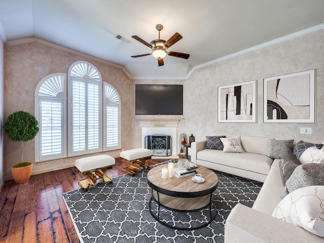 living room with hardwood / wood-style floors, lofted ceiling, a tiled fireplace, ceiling fan, and crown molding