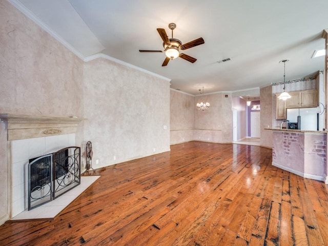 unfurnished living room with crown molding, light hardwood / wood-style floors, a tiled fireplace, and ceiling fan with notable chandelier