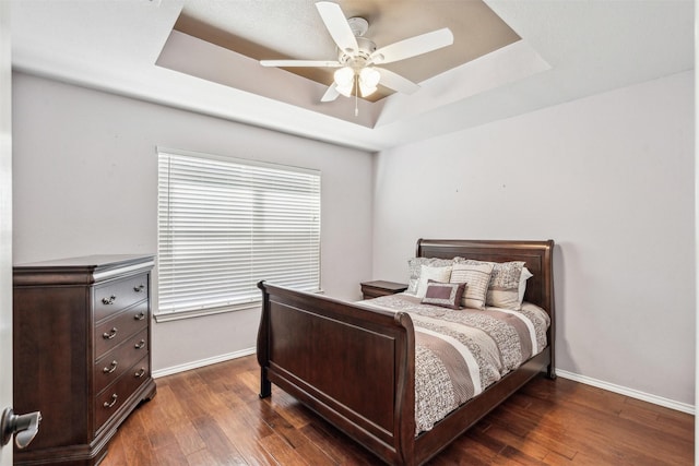 bedroom featuring dark wood-type flooring, ceiling fan, and a tray ceiling