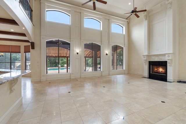 unfurnished living room with a high end fireplace, beam ceiling, a towering ceiling, and ceiling fan