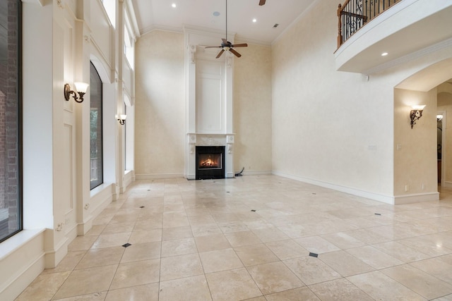 unfurnished living room with ceiling fan, light tile patterned flooring, a towering ceiling, and crown molding