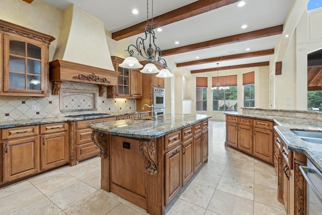 kitchen with pendant lighting, a center island with sink, dark stone countertops, beam ceiling, and custom range hood