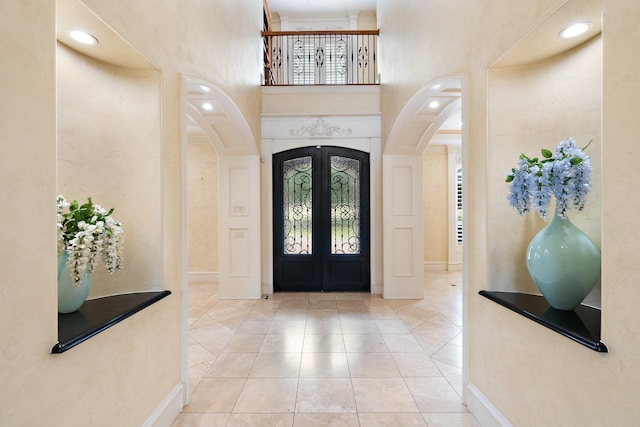 foyer with french doors, light tile patterned floors, plenty of natural light, and a high ceiling