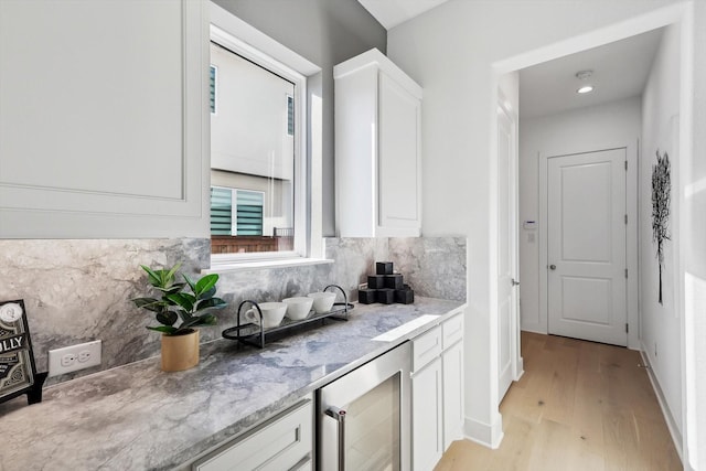 kitchen featuring light stone countertops, light wood-type flooring, white cabinetry, and beverage cooler