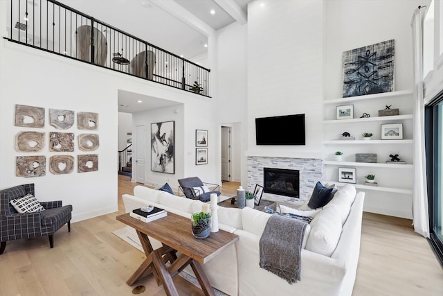 living room with a towering ceiling, beam ceiling, built in features, a fireplace, and light hardwood / wood-style floors