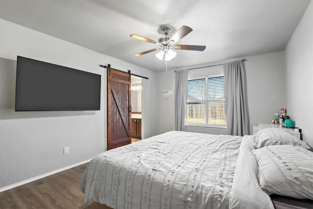 bedroom with a textured ceiling, a barn door, dark hardwood / wood-style floors, and ceiling fan