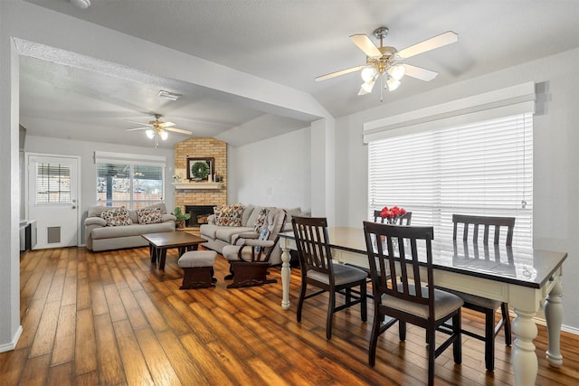 dining area with vaulted ceiling, ceiling fan, dark hardwood / wood-style floors, a textured ceiling, and a fireplace