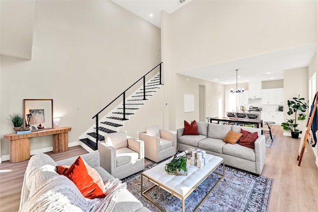 living room with a towering ceiling, light wood-type flooring, and a notable chandelier