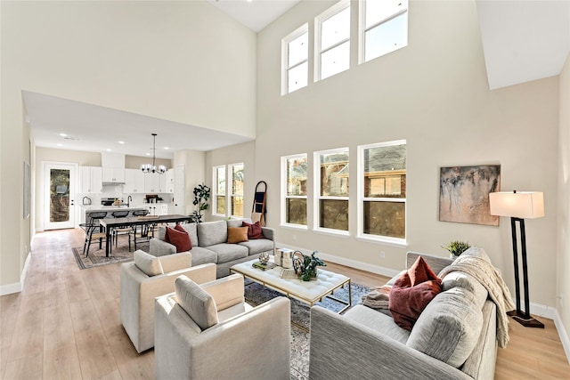 living room featuring an inviting chandelier, a towering ceiling, and light hardwood / wood-style flooring