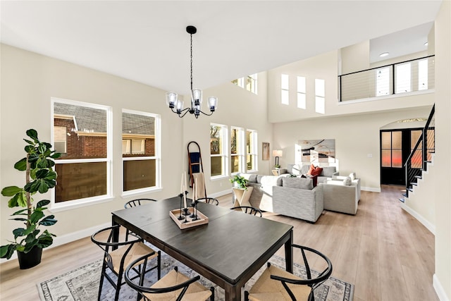 dining area with a notable chandelier, a towering ceiling, and light hardwood / wood-style floors