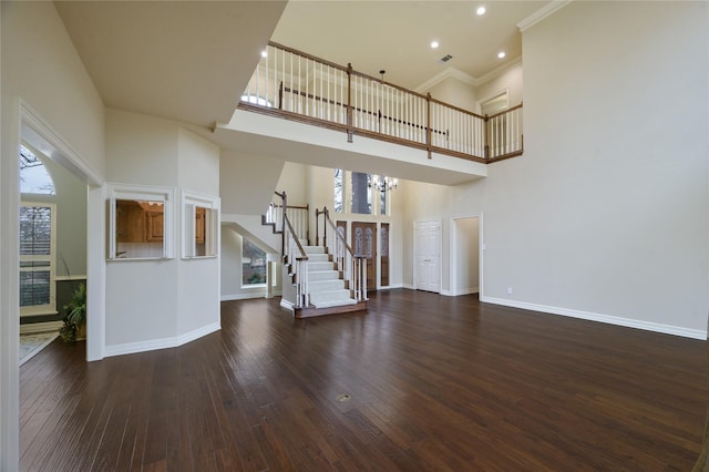 unfurnished living room with a high ceiling, an inviting chandelier, crown molding, and dark wood-type flooring