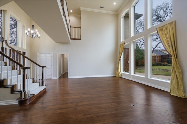 unfurnished living room with crown molding, a towering ceiling, dark hardwood / wood-style floors, and an inviting chandelier