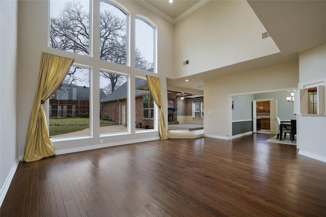 unfurnished living room with crown molding, a towering ceiling, ceiling fan with notable chandelier, and dark hardwood / wood-style floors