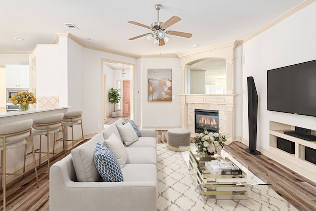 living room featuring a fireplace, crown molding, light hardwood / wood-style flooring, and ceiling fan