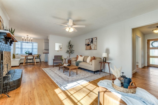 living room featuring a brick fireplace, ceiling fan with notable chandelier, crown molding, and light hardwood / wood-style flooring