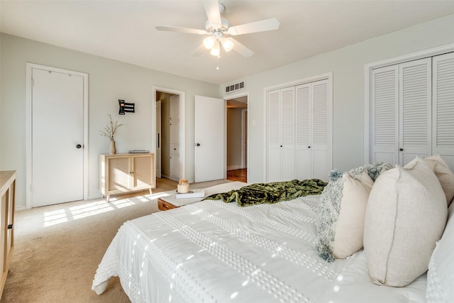 bedroom with light carpet, ceiling fan, and multiple closets