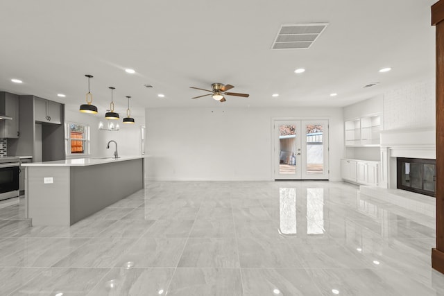 unfurnished living room with ceiling fan, sink, a fireplace, and french doors