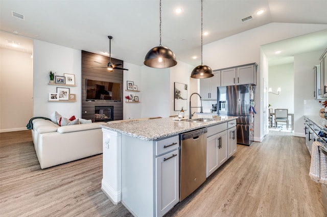 kitchen featuring a kitchen island with sink, sink, ceiling fan, appliances with stainless steel finishes, and light stone counters