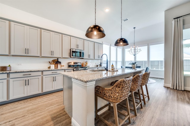 kitchen with sink, hanging light fixtures, light wood-type flooring, an island with sink, and stainless steel appliances