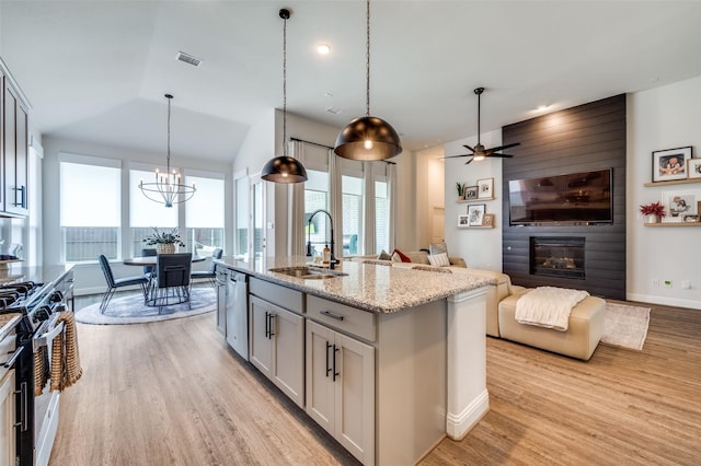 kitchen featuring light stone countertops, appliances with stainless steel finishes, sink, pendant lighting, and an island with sink