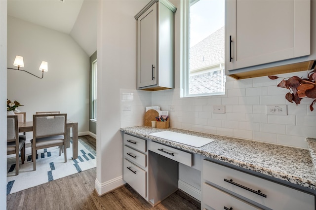 kitchen featuring decorative backsplash, light hardwood / wood-style flooring, light stone counters, and lofted ceiling