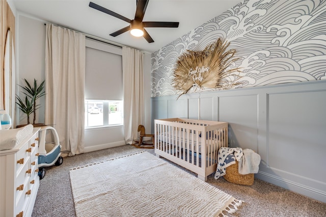 carpeted bedroom with ceiling fan and a nursery area