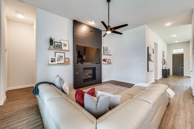 living room with ceiling fan, a large fireplace, and wood-type flooring