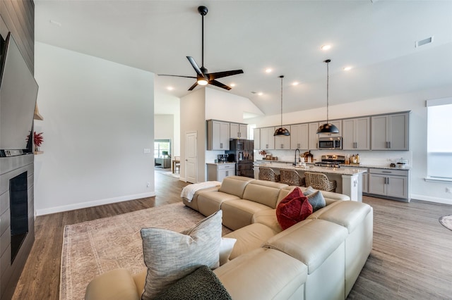 living room featuring dark hardwood / wood-style floors, ceiling fan, sink, and high vaulted ceiling