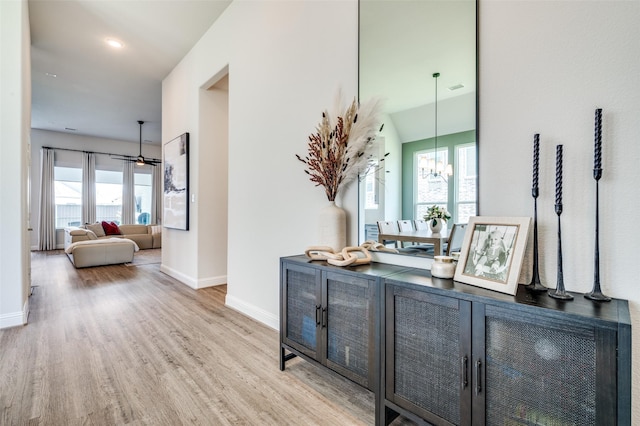 hallway with a wealth of natural light, light hardwood / wood-style flooring, lofted ceiling, and an inviting chandelier