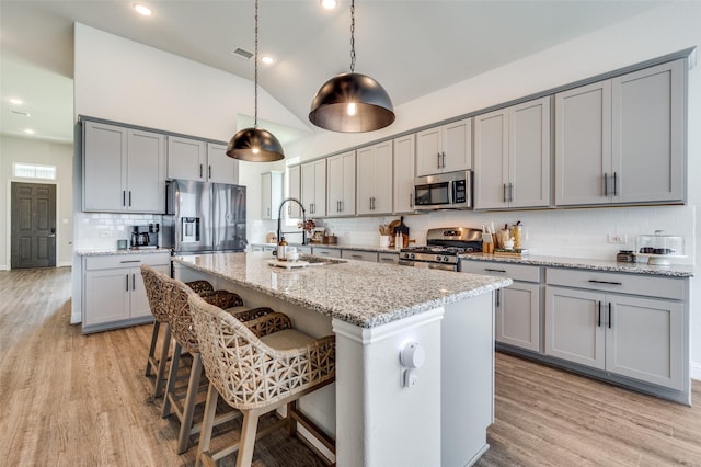 kitchen featuring a kitchen island with sink, appliances with stainless steel finishes, tasteful backsplash, decorative light fixtures, and light stone counters